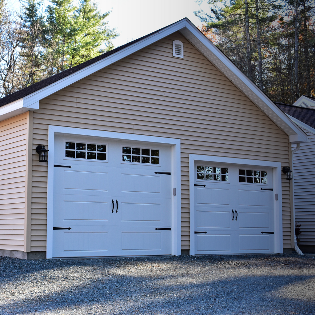 Two-car garage with white doors and beige siding, surrounded by trees.