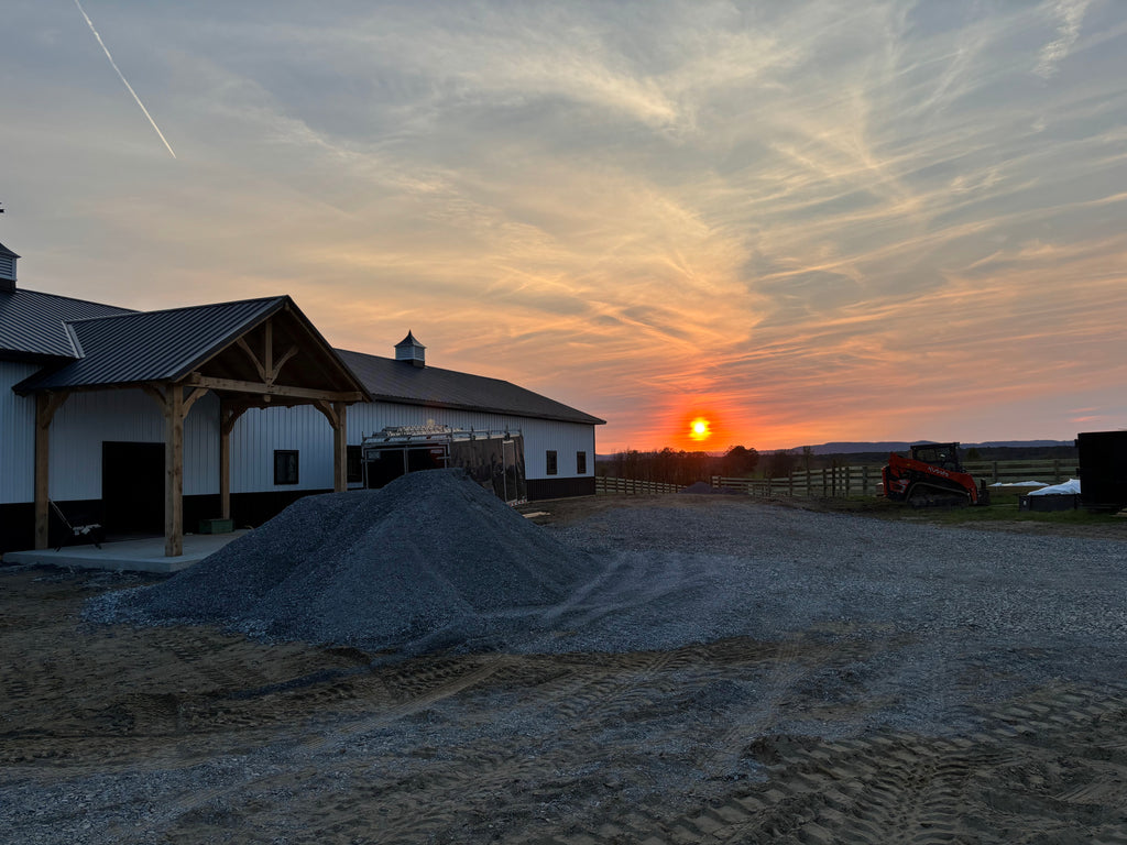 Sunset over a farm with a barn and equipment.